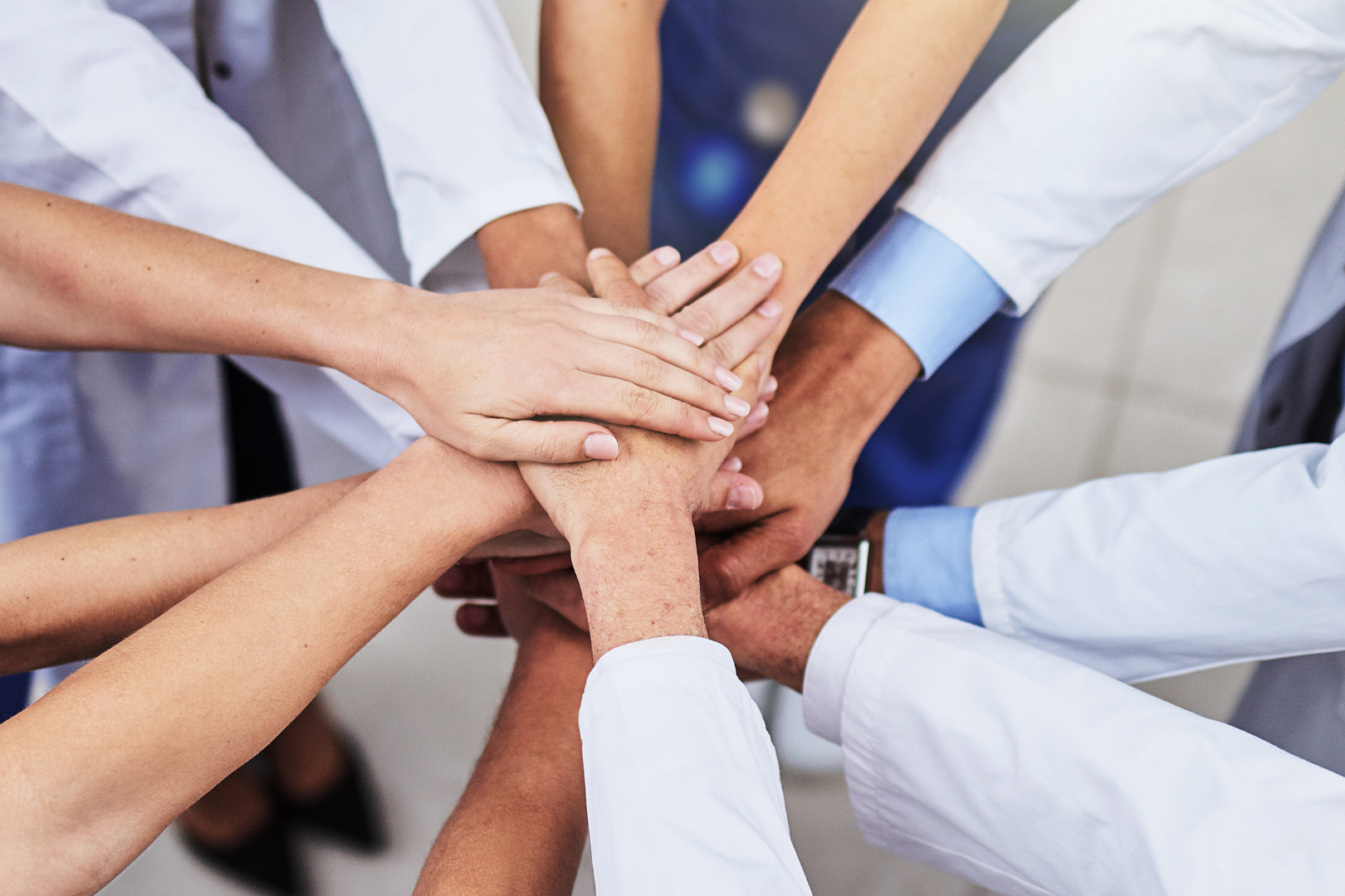 Team of people in white coats stacking hands in a circle to show teamwork and unity to support a common goal.