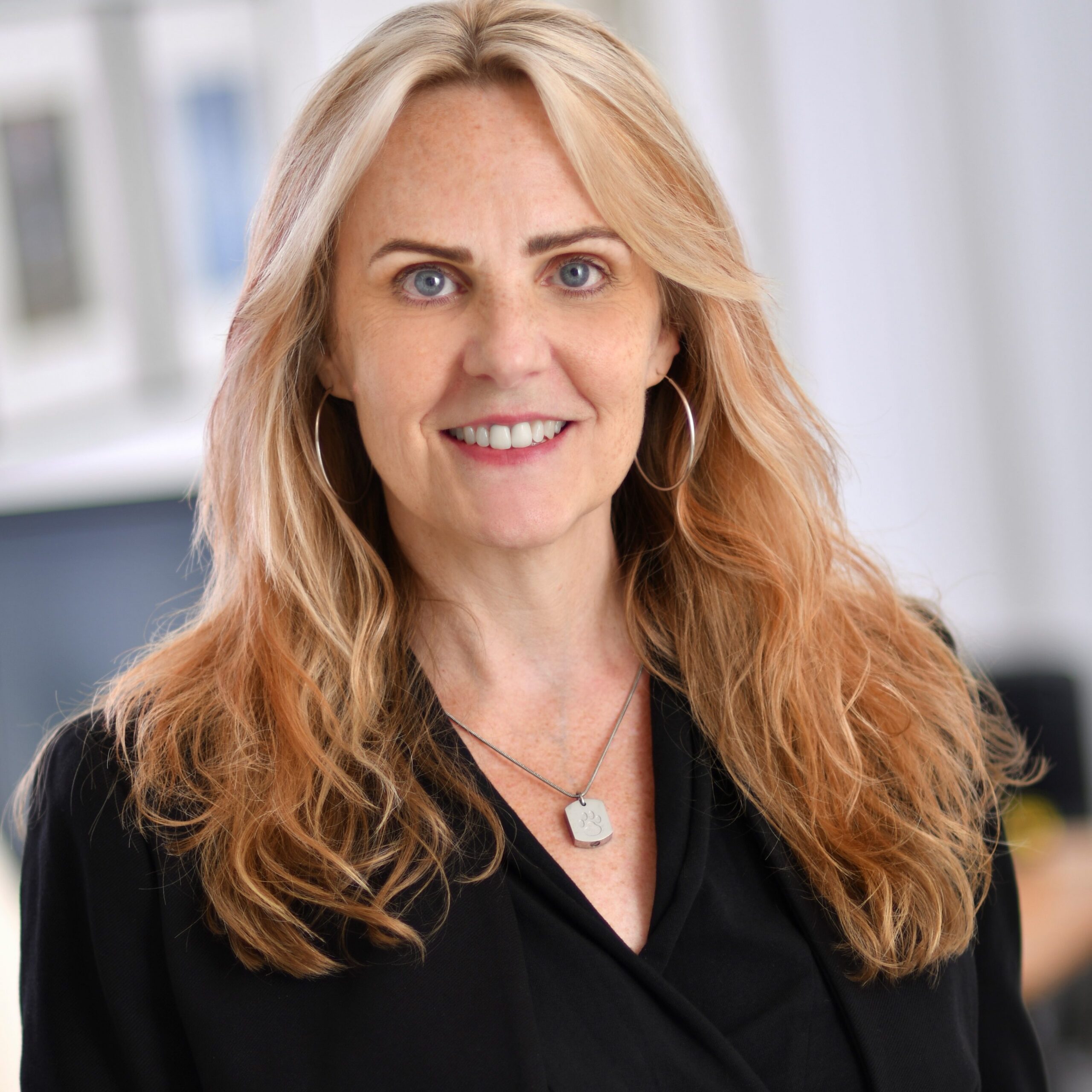 PamelaJoJohnson | PHF Smiling woman with long blonde hair wearing a black top and silver necklace outdoors