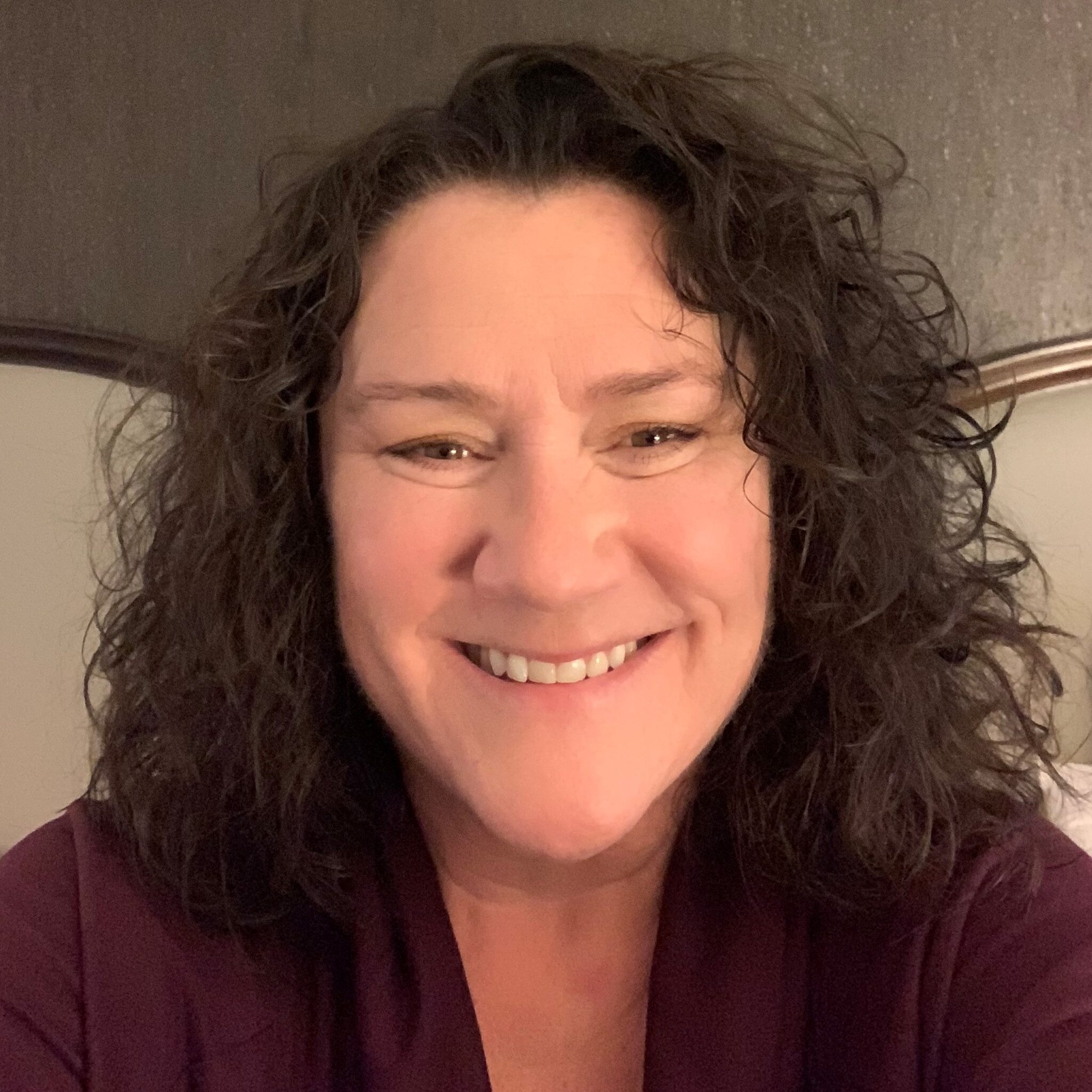 Tracy Miller | PHF Close-up of a smiling woman with curly dark hair and a maroon top, against a neutral background.